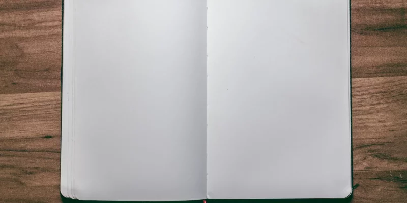 Ein geöffnetes Notizbuch mit leeren Seiten liegt auf einem Holztisch