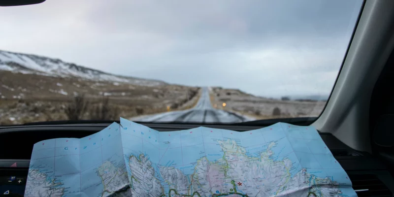 Eine Landkarte aufgefaltet auf dem Armaturenbrett eines Autos. Im Hintergrund windet sich eine Straße.