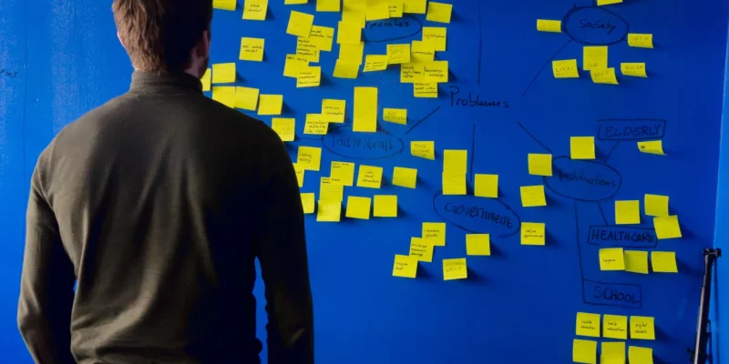 Eine Person steht vor einer blauen Wand, auf der viele gelbe Zettel kleben